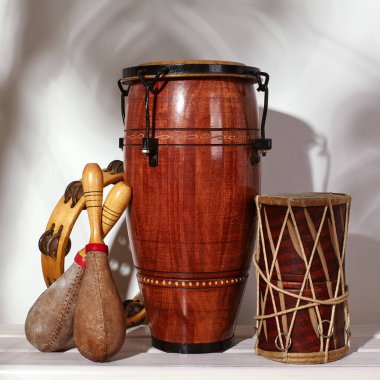 Etnik müzik enstrümanının kompozisyonu. Marakas, tef, konga ve etnik davul. Perküsyon ritim enstrümanları beyaz arka planda ve palmiye gölgesinde. Küba müziği, Latin kültürü, samba ve rumba