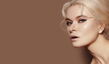 Geçmişe dönük makyajlı, temiz tenli, bej arka planda sarı saçlı güzel seksi bir manken. Moda makyajlı, saç stili zarif bir kadın. Boşluğu kopyala