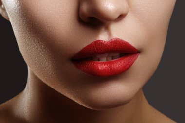 Stüdyo yakın plan, parlak kırmızı rujlu, hafif ışıklı dudak dokusu ve hafifçe gülümseyen dişleri olan bir kadın. Kozmetik reklamları ve güzellik makaleleri için ideal..