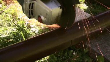 Açık havada elektrikli öğütücüyle metal boru kesimi, parlak uçan kıvılcımlar güç, inşaat ve onarım enerjisi gösteriyor. İşçilik, sıcaklık ve sanayi. Ağır işçilik. Metalurji veya araçlar için.