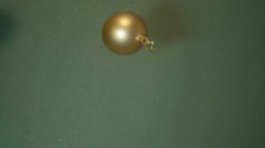 Altın Noel ağacı takıları yeşil bir zemine düşer, bayram neşesini, lüksü ve kış tatili ruhunu sembolize eder. Noel süslemeleri yuvarlanır ve ışıldar. Xmas kartı.