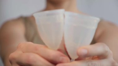 Yakın plan kadın elinde regl bardağı gösteriyor. Kadın hijyen ürünleri, çevresel sorumluluk ve öz farkındalık. Günlük bakım ve kadın döngüsü. Kadın sağlığı, adet görme ya da adet görme.