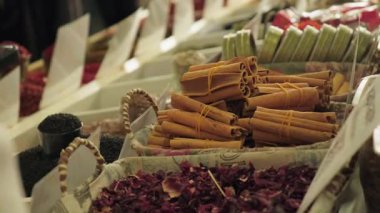 Baharatlı renkli market tezgahı, yakın plan tarçın, biber, hasır sepetlerde kurutulmuş gül yaprakları. Yerel piyasa, küçük işletmeler. Alışverişçilerin bulanık görüntüleri, hareketli akşam piyasası.