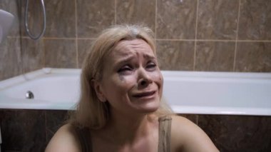 Kadınlara karşı şiddet, zihinsel bozukluk, yalnızlık ve korku kavramı. Sarışın kadın küvette ağlıyor, rimel lekeleri, akan gözyaşları, kederli bakışlar, fayanslı banyo arka planı, umutsuzluk, depresyon