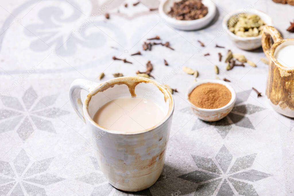 Masala chai served with cinnamon sticks, green cardamom seeds and anise over grey texture background