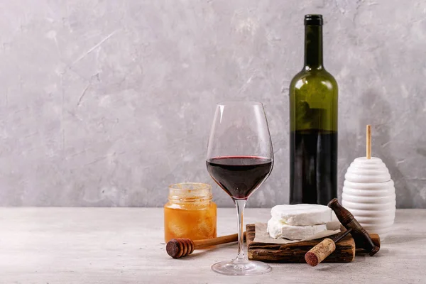 Goat cheese served with honey and bottle of red wine over white texture background. Copy space