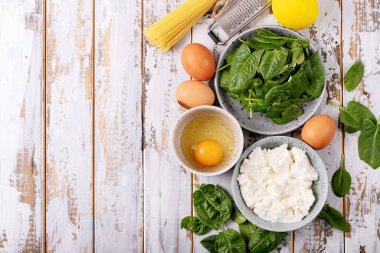 Beyaz ahşap zemin üzerinde ricotta peyniri, yumurta ve ıspanakla servis edilen ev yapımı tagliatelle vejetaryen yumurtalı makarna. Üst manzara, düz yatış. Boşluğu kopyala