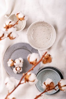 Akşam yemeği. Beyaz tekstil arka planında pamuk çiçeğiyle süslenmiş mavi, modern bir seramik tabak. Üst manzara, düz yatış. Herhangi bir ürün için yer. Yaratıcı yerleşim