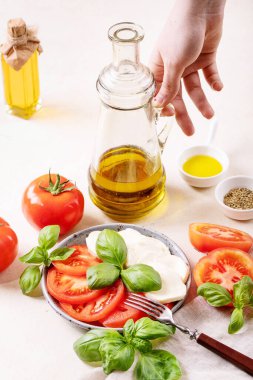 Ev yapımı sağlıklı yemek konsepti: kiraz domatesleri, mozarella topları, baharatlar, taze fesleğen ve zeytinyağlı cam şişe tutan kadın. Beyaz desenli Mozzarella salatası. Boşluğu kopyala