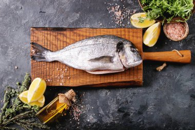 Çiğ, içi çiğ deniz kepeği ya da limon, yeşil salata, biberiye, zeytin yağı ve ahşap kesim tahtasının üzerinde koyu dokuya sahip pembe tuz ile servis edilen dorado balığı. Düz yat, boşluğu kopyala.