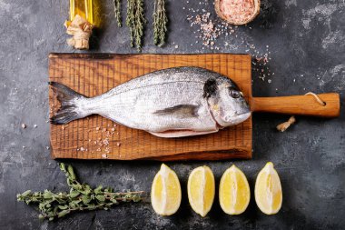 Çiğ, içi çiğ deniz kepeği ya da limon, yeşil salata, biberiye, zeytin yağı ve ahşap kesim tahtasının üzerinde koyu dokuya sahip pembe tuz ile servis edilen dorado balığı. Düz yat, boşluğu kopyala.