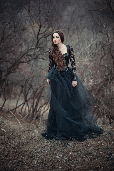 Beautiful girl with long hair standing in a black dress standing on the gothic background blowers forests, forest princess, halloween , dark boho , fashionable toning , creative color