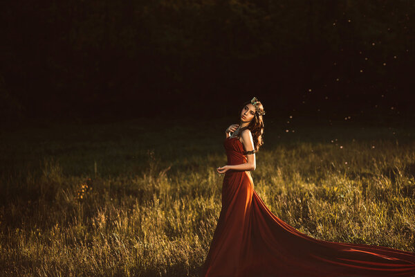 Beautiful young princess in a long red dress walks among the green plants in the woods , a fashionable toning , creative color