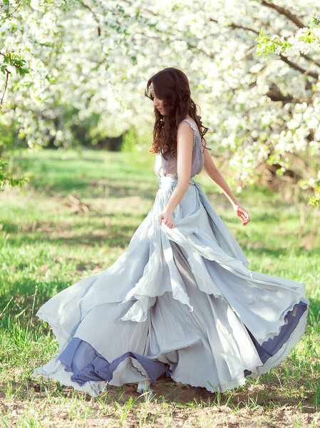 Beautiful spring walk in the garden among the blooming trees in April a lady in a long dress pastel , creative computer colors, fashionable toning