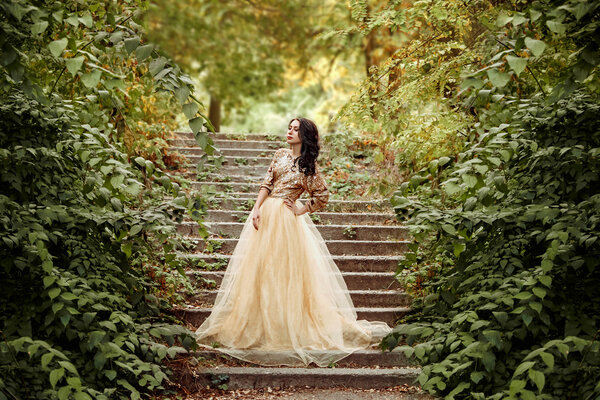 Beautiful girl in a luxurious dress walks in autumn park near the castle.Princess sits on the steps of the fall of the castle.Fashionable toning.creative colors