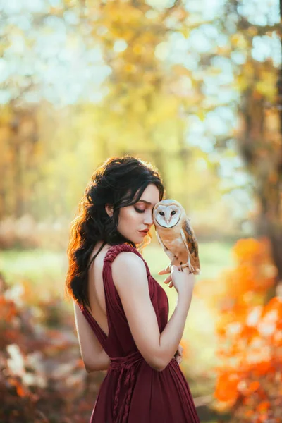 Helder herfst sprookje. Fantasie vrouw knuffelt een schuur uil. Bos nimf meisje houdt een witte vogel in haar handen. Portret van een romantische dame in een creatieve jurk. Achtergrond van de natuur, oranjegele bomen — Stockfoto