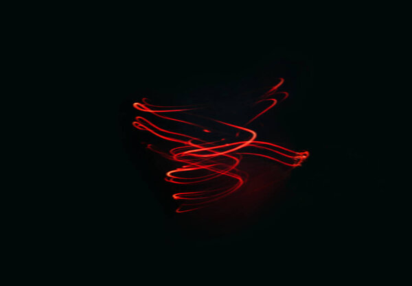 Red glowing spiral of red color on a black background. Creative texture, smooth lines swirl, movement on dark backdrop. Long exposure mixed light shooting. Creative futuristic desktop wallpaper