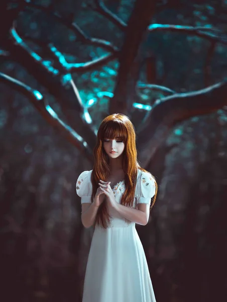 Fiatal, gyönyörű, vörös hajú lány, egy misztikus sötét, sűrű erdőben áll, imádkozva összehajtogatva. Éjszakai háttér, fa hold fény. Fehér, hosszú vintage ruha. Félelmetes középkori hercegnő lány.. — Stock Fotó