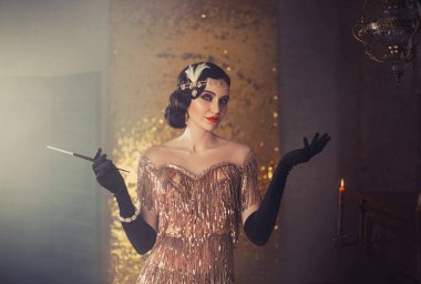 portrait of retro flapper beauty fashion model. Woman holding long slim mouthpiece in hand, cigarette. Party 20s style room full smoke. Gold shiny dress, accessories. Invitation gesture, free space clipart