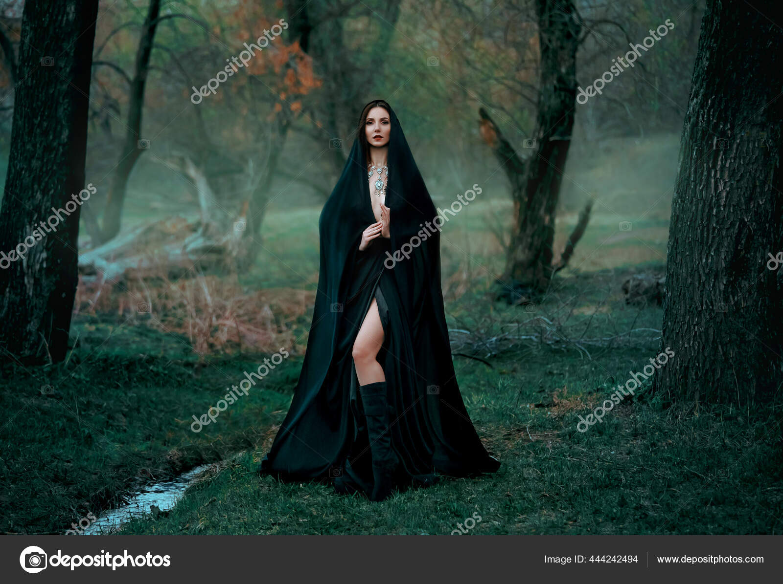 Scary young female in colorful contact lenses and with painted face  standing in dark forest and