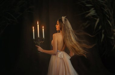 Fantezi ortaçağ kızı prenses karanlık gotik odada yürüyor. Kadın kraliçe elinde mumlarla şamdan tutuyor. Sırtı açık giyinmiş, uzun sarı saçları havada uçuyor. Git buradan.
