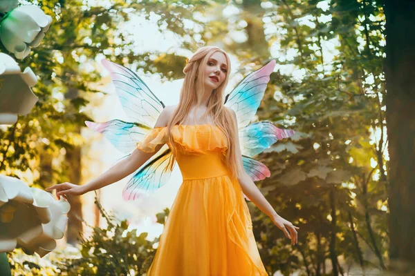 ポートレートファンタジー女性ブロンドの森妖精。明るい黄色のドレスでエルフの女の子のファッションモデル、蝶の翼。ピクシーは夏の自然を歩く。緑の春の木、木、太陽の光魔法の輝き。長い髪 — ストック写真