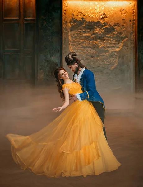 Любящая пара танцует на балу фей. Счастливая женщина фантазии принцесса в желтом платье и парень заколдованный зверь, рога на голове Девушка кружится в руках мужского принца. Карнавальный костюм человека-монстра — стоковое фото
