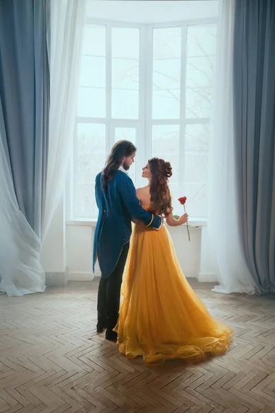 Feliz pareja abrazo en la habitación blanca viejo castillo cerca de la ventana. Feliz belleza sexy mujer princesa de fantasía en vestido amarillo y hombre príncipe. Romántico rey masculino abraza chica. Arte Vintage estilo traje vista trasera. — Foto de Stock