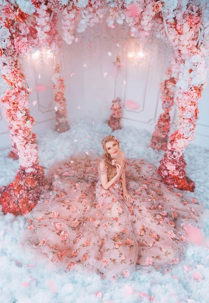 Mulher feliz de primavera de fantasia em vestido longo. Saia de tecido em flores. Criativa arco rosa rosa rosas brancas. Pétalas a cair. Fada princesa menina sentada no inverno cenário de neve, sala de decoração de arte. Modelo de moda — Fotografia de Stock