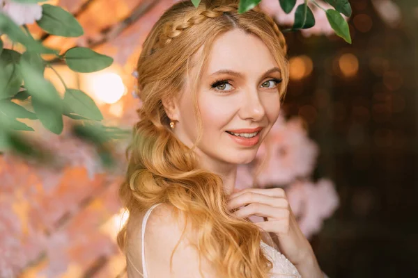 Portrait of young happy beautiful blonde woman in white vintage dress. Girl laughs smile on face. Studio background, blooming pink sakura tree. Long hair is braided into an elegant romantic hairstyle — Stock Photo, Image