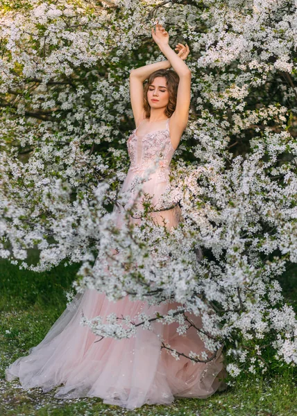 Elegant adult girl fashion model posing. Lady in pink evening dress. Elegant romantic woman enjoying spring nature. Green blooming trees white flowers. Fantasy vintage lady in flowering blossom garden — Stockfoto