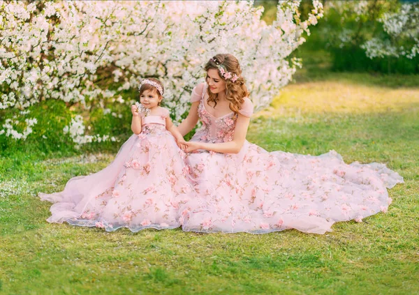 Young happy family, mom and daughter in beautiful evening festive long powdery pink color dresses. Woman holds little girl in hand, looks with love, smile on face. Wedding lush outfits. fashion model.