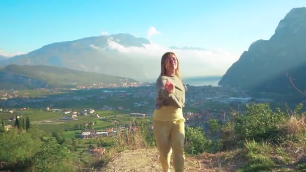 Alegre alegre alegre jovem turista dançando pulando cabelo longo voando alegremente lança. Menina girando as mãos levantadas rosto sorridente. Vista superior Riva del Garda montanhas dolomites céu azul Itália Alpes. — Vídeo de Stock