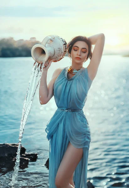 Φωτογραφία τέχνης. Πορτρέτο μυθικό κορίτσι Ελληνίδα θεά. Αστρολογικό ζώδιο Υδροχόος. Φανταστική γυναίκα χύνει νερό από κεραμική πήλινη κανάτα. Μπλε σιφόν παλιό εκλεκτό μακρύ μεταξωτό φόρεμα. υπέροχη λίμνη, μαγικό ηλιοβασίλεμα — Φωτογραφία Αρχείου
