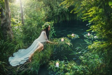 Fevkalade efsanevi doğal manzara. Ormandaki fantezi kadın kıyı gölünde oturur, peri kızı suya çelenk atar. Eski Slav tarikatı ayini Ivan Kupala. Uzun beyaz elbise. Siyah saçlı.