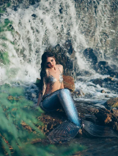 Mujer de fantasía verdadera sirena mito diosa del mar. Arte de plata oscura traje de baño sirena del océano sexy cuerpo. Reina del río lago. cola de pescado. Chica se sienta en la orilla del mar, cascada de fondo, salpicaduras de agua. — Foto de Stock