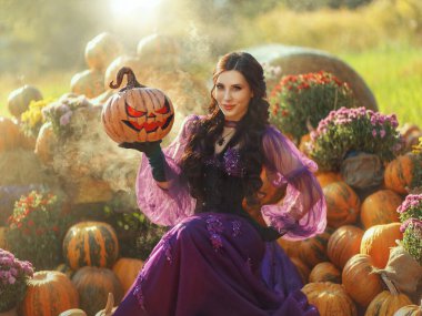 Sanat fotoğrafı gerçek insan mutlu güzel kadın turuncu balkabağı oymalı Jack O Lantern. Mutlu, mutlu, gülümseyen, gizemli kız, mor elbise. Cadılar Bayramı hasat balkabakları Şükran Günü