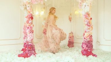 Dans eden, gülümseyen neşeli yüzlü sarışın kadın portresi. Pembe çiçekli elbisesini sallayan bahar perisi prenses kız. Beyaz oda şık gelin sarı saç, tatil düğün kemeri, resmi tören