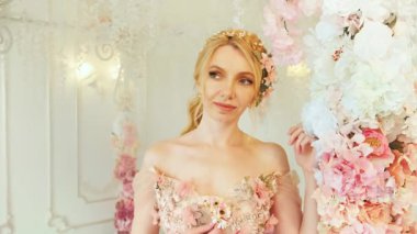 Beyaz oda bahar manzarasında mutlu, fantezi kadın prenses, çiçek dekoru. Kadın kraliçe sarışın, klasik pembe elbise romantik saç stili kamera modeli pozu, akşam balosu makyajı