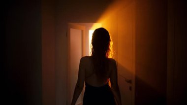 Baştan çıkarıcı kadın yatak odasına gider, açık siyah vücut silueti olan seksi elbiseler, karanlık odada yürürken pencereden gün batımını seyreder. Kapı açık. Kız model.