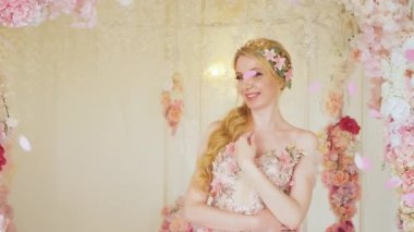 Fantezi portresi mutlu kadın prenses, çiçekli uzun gece elbisesi sarı saçlı saç tokası. Yukarıdan gül yaprakları düşer, bayram krakerleri. Gülen kız. Düğün gelini, kemer dekoru