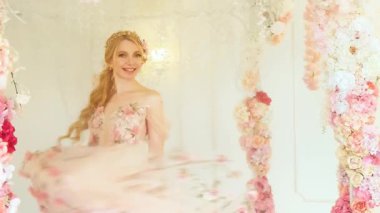 Portre fantezi sarışın kadın dans ediyor, gülümseyen neşeli yüz. Bahar perisinin tanrıçası prenses kız pembe lüks çiçekli elbisesini sallıyor. Beyaz oda. Şık gelin, sarı saç, klasik saç stili.