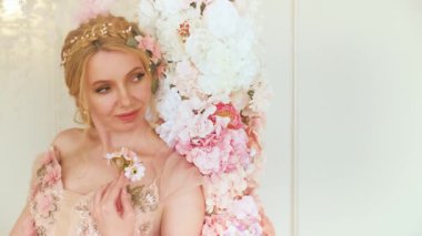 Dudakları yeşil, elleri kapalı, küçük buket pembe çiçekleri tutuyor, yaratıcı tasarım çiçek dekoru. Seksi, sarışın, uzun saçlı, güzel, sanat portresi. Fantezi tanrıçası kraliçe bahar çelengi tacı.