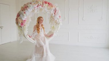 Mutlu gelin kadın salıncakta sallanıp aşkı bekliyor. Modaya uygun, uzun, şık, beyaz gelinlikli bayram kutlaması yapan bir kız. Sarı saçlar. Klasik oda çiçekli dekor sallanan sandalye