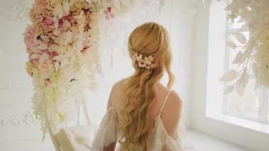 Mutlu gelin gelin sarışın çiçek salıncağına oturur. Kız manken seksi, arkası açık, şık beyaz gelinlik. Uzun sarı saçlar zarif gevşek düğün günü saç stili, dikiz manzarası.