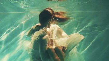 Mutlu fantezi çifti, yüzme havuzunda yüzen adama aşık olur. Kral ve kadın model, suyun altında koyu mavi deniz pozu verir. Islak beyaz elbise. Peri seksi kız ilham perisi nehir perisi sarılan adam havuzun altında 4 km yüzüyor.