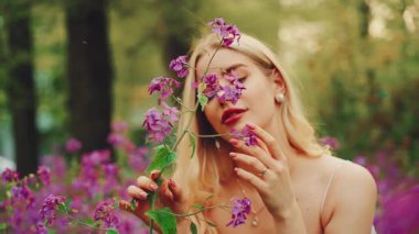 Portre güzeli gülümseyen kız peri masalı meleği. Genç, mutlu bir kadın, yaz mevsiminin tadını çıkarıyor. Boho tarzı beyaz elbise. Sarı saçlı seksi bayan çiçekli kokuyu soluyor.