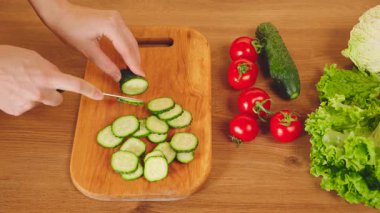 Yakın çekim insan elleri sağlıklı sebze diyeti yemeği için salatalıkları tahta tahtada kesiyor. Mutlu kadın ev hanımı kendini rahat hissediyor. Kahvaltıyı hazırlamaktan hoşlanıyor. Mutfakta taze salata.