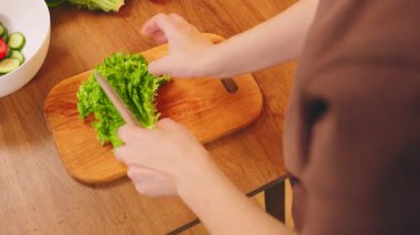 Yakın plan insan eli, sağlıklı sebze diyeti yemeği için tahta tahtada parlak marul yaprakları kesiyor. Mutlu kadın vejetaryen kahvaltısı hazırlıyor taze yeşil salata kâseye dökülüyor..