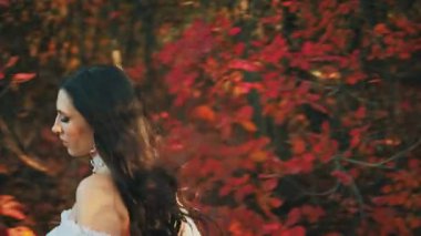 Gizemli fantezi kadın ormanda koşuyor. Prenses kız güzellik suratı. Beyaz, uzun, ipek kumaşlı kumaş rüzgarda uçuşuyor. Arka taraftaki bayan patikadan kaçtı. Sonbahar doğası kırmızı yapraklar